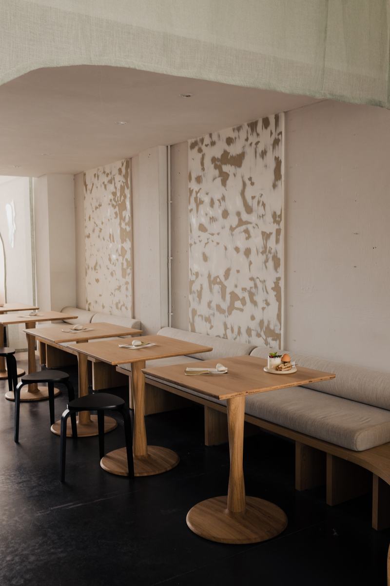 Houten tafels, zwarte krukken en een lange zitbank onder de wandkunst