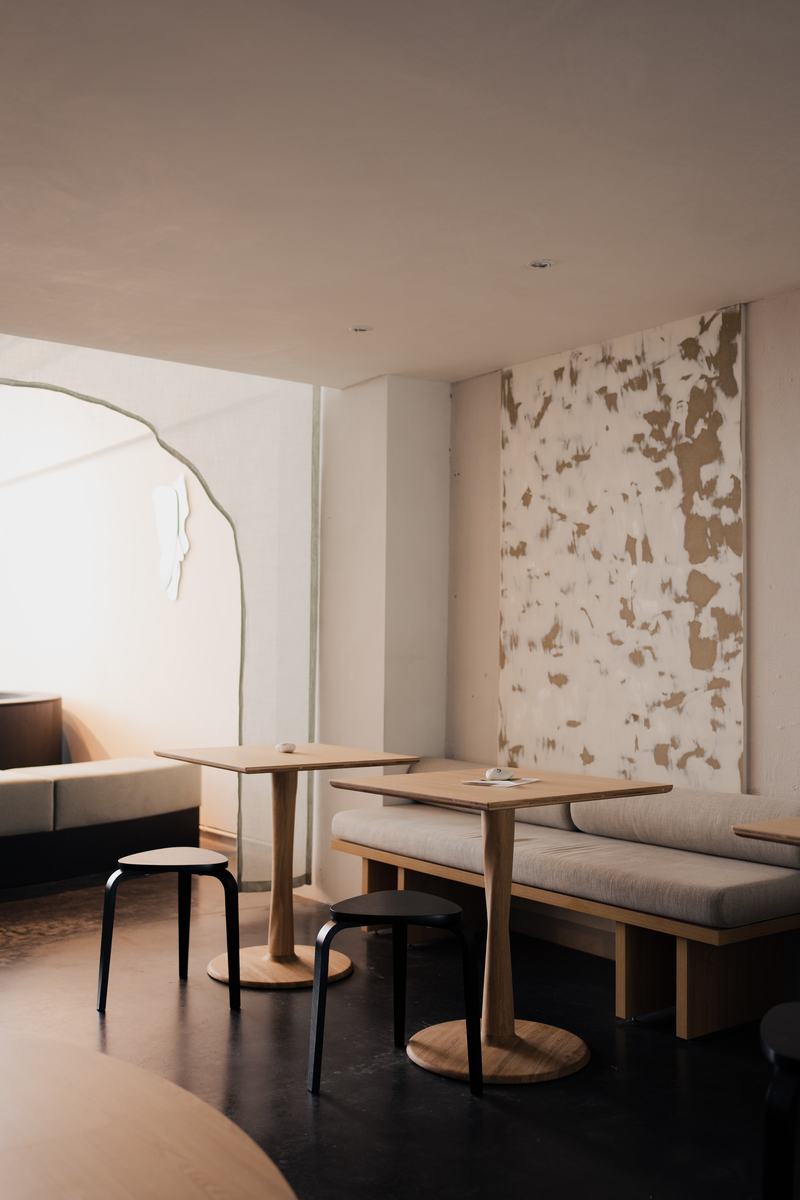 Houten tafels en een zitbank bij de wandkunst, met de boog links